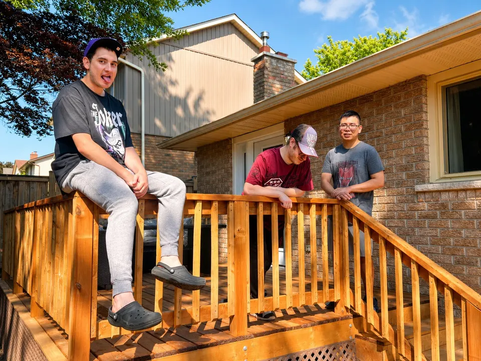 A young man sitting on the deck steps outside his home in the sunshine