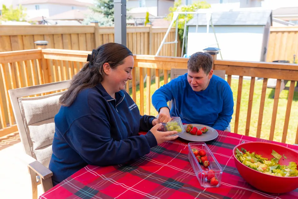 A support worker and a man sharing a plate of fruit at the table on the back deck