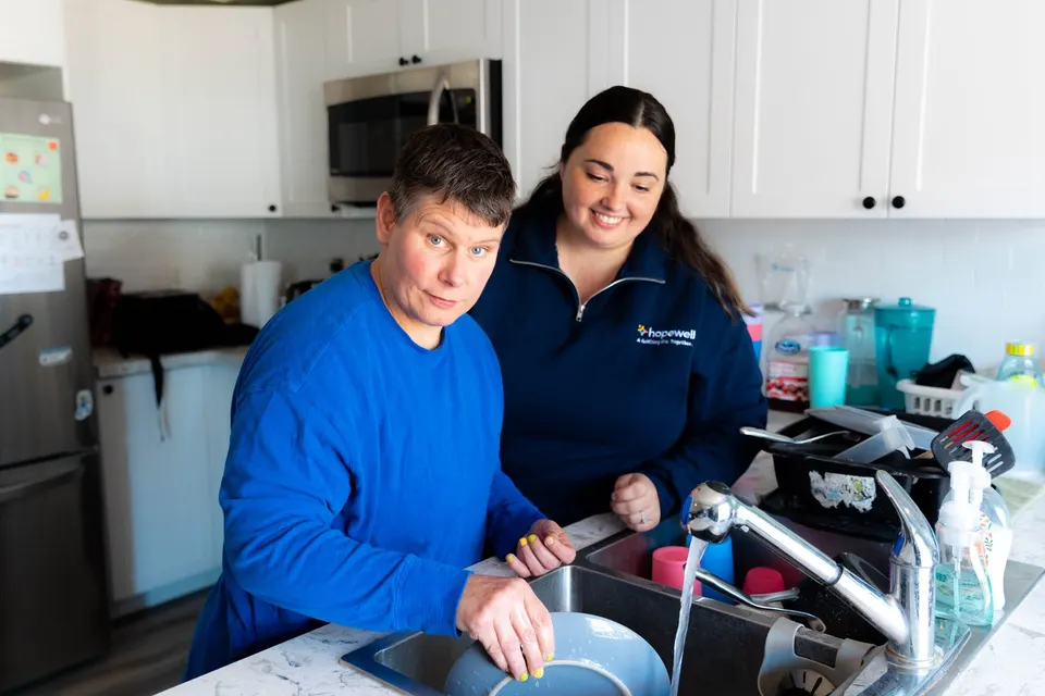 A woman and a support worker washing dishes side by side at the kitchen sink of a Hopewell home