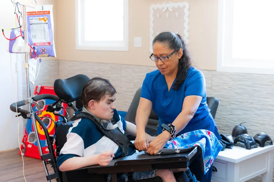 A nurse working closely with a young person in a specialized wheelchair at home