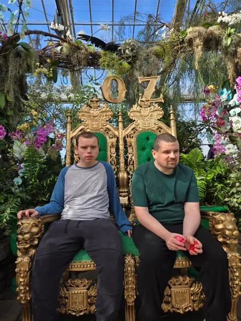 Two men sitting on ornate golden thrones at a themed community attraction