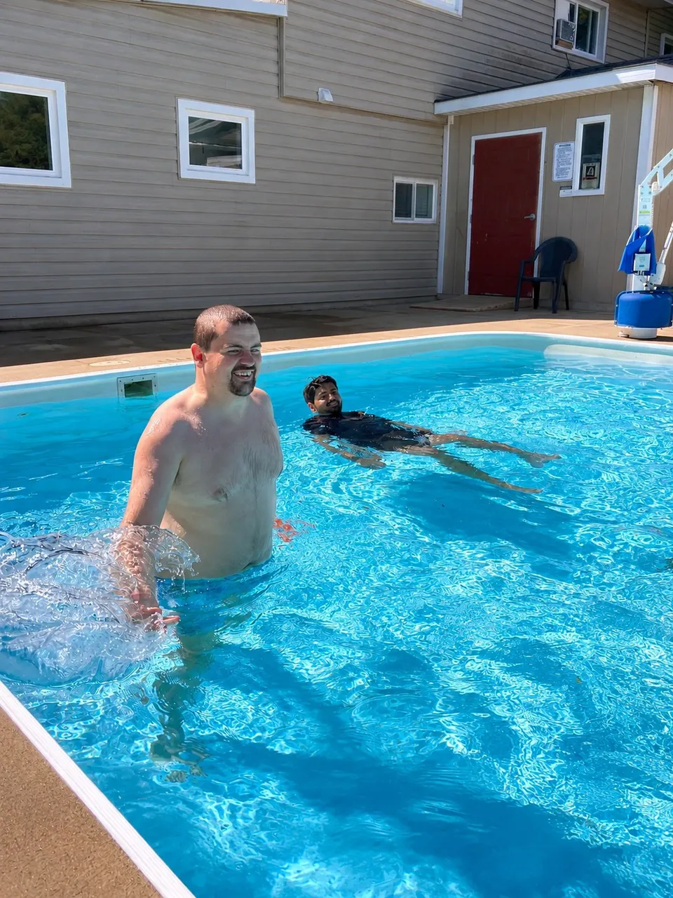 A man swimming in the pool with a support worker close by