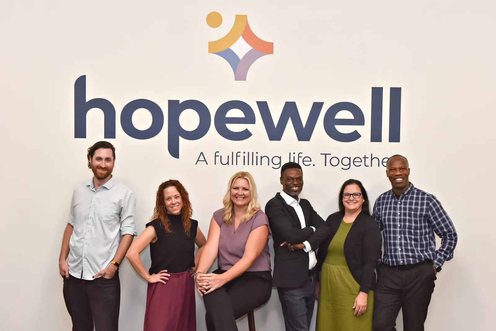 Six members of Hopewell's senior leadership team standing together in front of the Hopewell logo at the Guelph office.