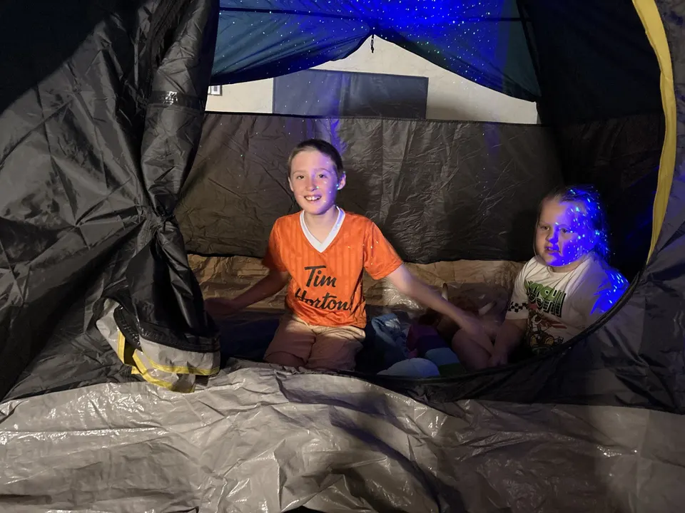 Two children sitting inside a camping tent lit by a starry night-sky projector at a Youth Connect camp.