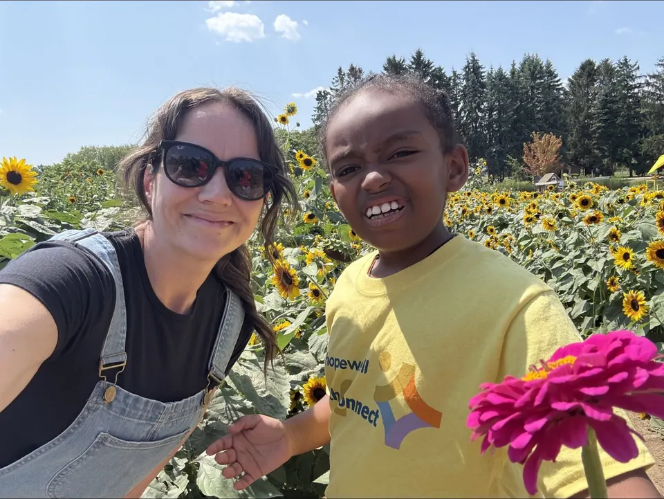 A support worker and a child smiling together in a field of sunflowers on a Youth Connect community outing.